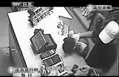 戴帽男子一手掐住加油站營(yíng)業(yè)員，一手持發(fā)令槍指向另一營(yíng)業(yè)員，要求“把錢給我裝起來”。