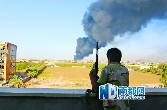 2日，利比亞首都的黎波里，一民兵武裝成員眺望被火箭彈擊中的儲油罐冒出濃煙。