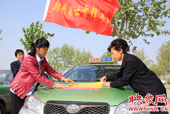 　　授旗結(jié)束后，首都的士雷鋒車隊王鳳進隊長（右）與鄭州的的哥的姐在車身上貼上標識。