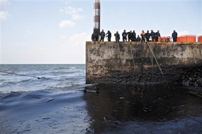 昨日，山東青島，清污人員正在海邊清理油污。