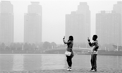 29日中午，鄭東新區(qū)如意湖畔，兩個(gè)年輕人拍攝霧霾中的景色。 鄭州晚報(bào)記者 馬健 圖