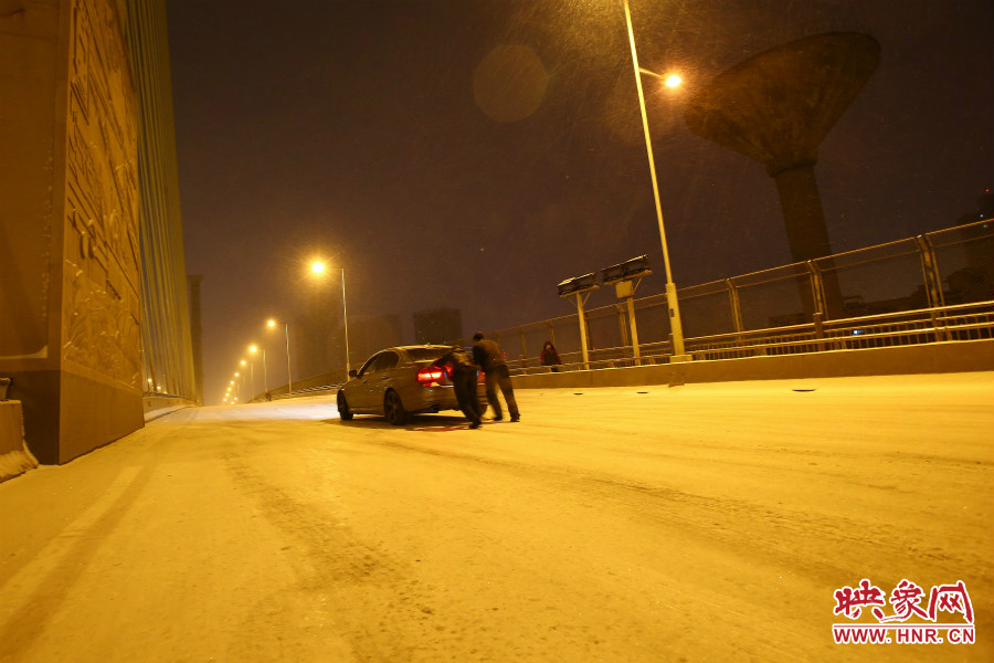 雪天路滑，汽車上橋打滑，兩名“推車人”幫助一輛私家車上坡。