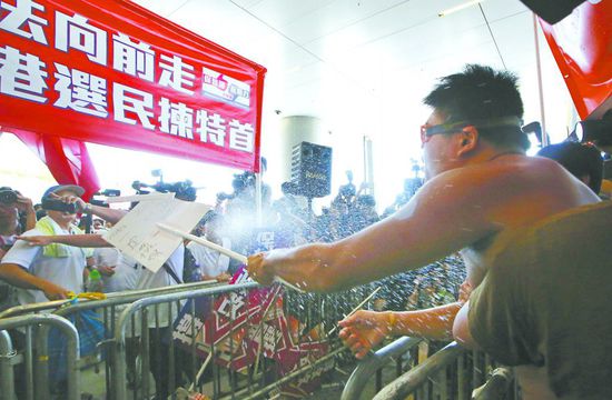 17日，在香港立法會外，一名反對政改的男子向支持派人群投擲標牌。