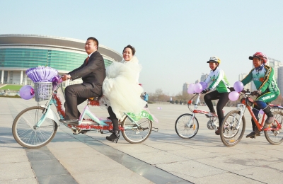氣球和鮮花裝點(diǎn)的雙人自行車，新郎郝幸福載著美麗新娘回家。