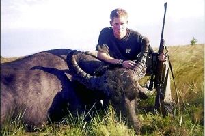 哈里王子手持獵槍，蹲在一頭遭到獵殺的水牛旁邊