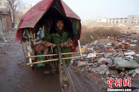 圖為老人走出窩棚，推著三輪車準(zhǔn)備出去撿拾廢品。周小云 攝